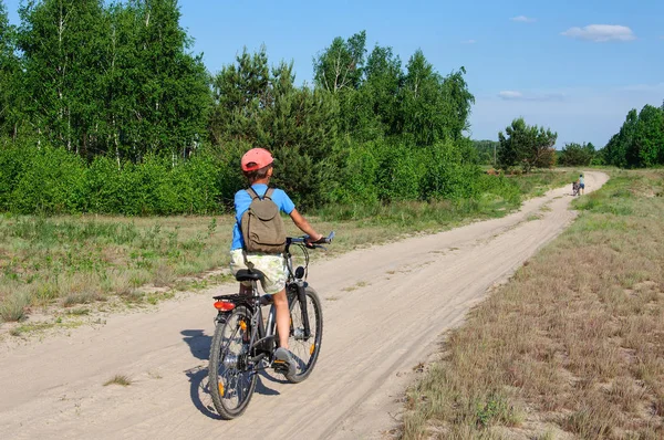 Menino de sete anos em um passeio de bicicleta esportiva ao longo de uma estrada de terra contra o céu azul — Fotografia de Stock