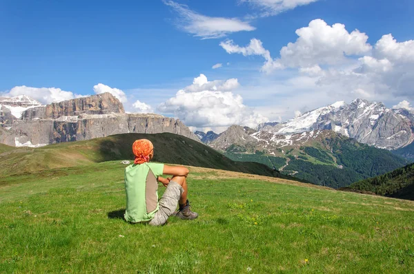 Молодой человек сидит на зеленой лужайке и смотрит на заснеженные доломиты, Италия. — стоковое фото