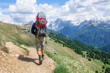 Bir sırt çantası küçük çocuk ile baba karla kaplı Dolomitler boyunca yürür, Italya.