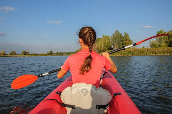 一个穿着粉色T恤的女人在河边的一艘红色皮划艇上划桨 乌克兰 — 图库照片