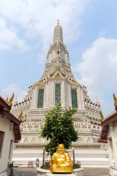 Golden statue of sitting Buddha and decorated Wat Arun temple viewed from the front in Bangkok, Thailand, on a sunny day.