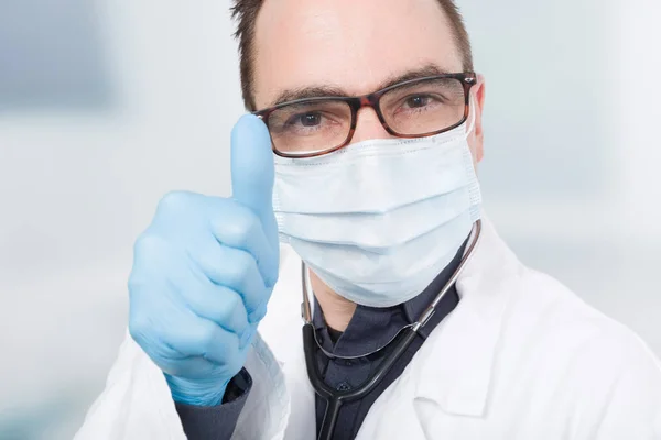 doctor with medical face mask and hygienic gloves shows thumb up
