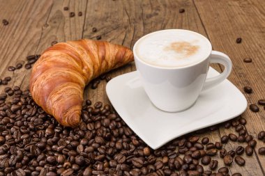 fincan Cappuccino ve ahşap masa üzerinde kahve çekirdekleri
