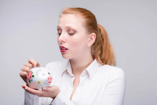 Junge rothaarige Frau steckt eine Münze in ihr Sparschwein — Stockfoto