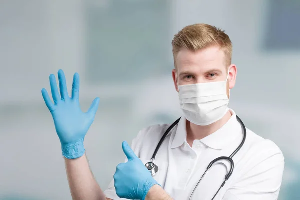 Arzt Mit Medizinischer Gesichtsmaske Und Stethoskop Zieht Medizinische Handschuhe Und — Stockfoto