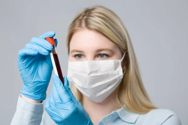 young woman with medical gloves and medical face mask holding a blood probe