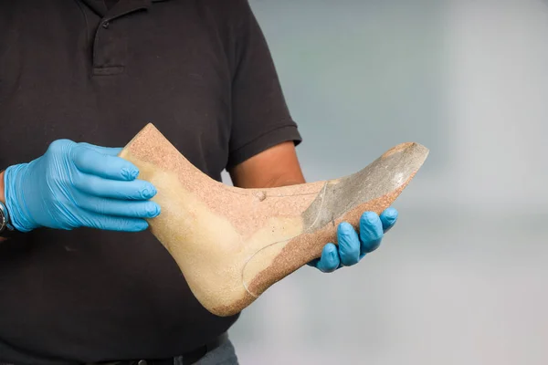 Close up of hands of an orthopedic shoemaker presenting an individual crafted wooden last