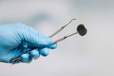 Dişçinin elinde mavi eldivenler ve iki diş aleti var. 