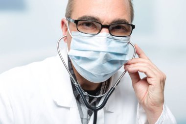 doctor with medical face mask and medical gloves in front of a clinic room clipart