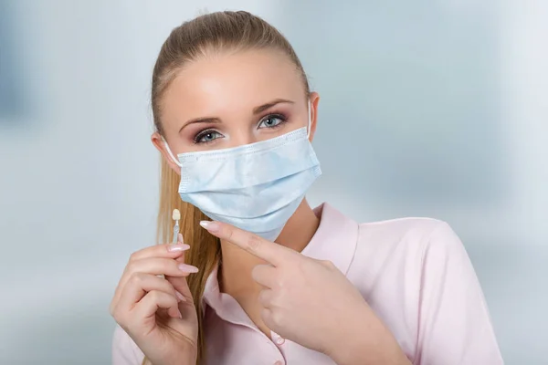 歯医者の助手 歯医者の顔のマスクを持つ女性歯科医は歯の通気口をチェックするための日陰ガイドを提示します — ストック写真