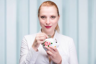 Genç kızıl saçlı kadın kumbarasına / porselenine bozuk para koyuyor.