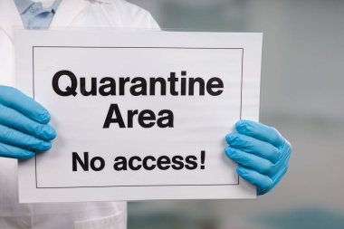 Doktorun elinde tıbbi eldiven var. Önünde karantina işareti var.