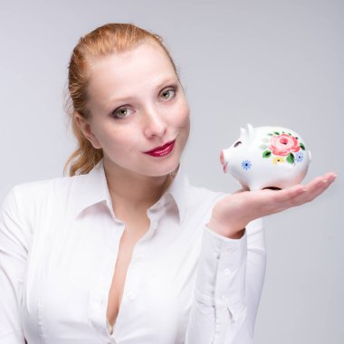 Genç kızıl saçlı kadın kumbarasına / porselenine bozuk para koyuyor.