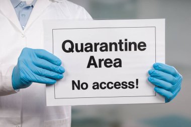 Doktorun elinde tıbbi eldiven var. Önünde karantina işareti var.