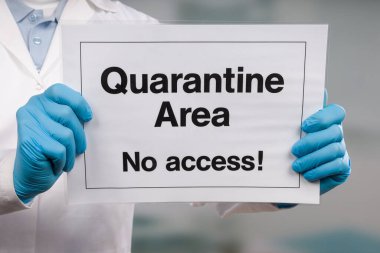 Doktorun elinde tıbbi eldiven var. Önünde karantina işareti var.