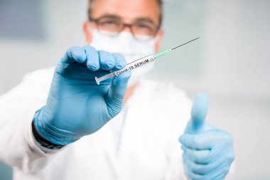 Eldivenli ve maskeli bir doktor Covid-19 aşısı olan bir şırınga gösteriyor.