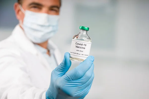 doctor with gloves and face mask presenting a bottle / flask with Covid-19 serum / vaccine