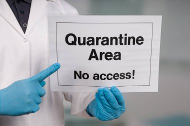 Doktorun eli tıbbi eldivenlerle klinik odasının önündeki karantina işaretini gösteriyor.