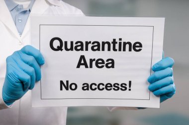Doktorun elinde tıbbi eldiven var. Klinik odasının önünde karantina işareti var.