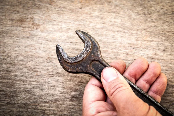 Old and rusty wrench in hand on wooden background