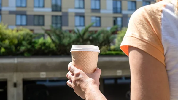 Holding takeaway coffee cup, apartament and office building in the background