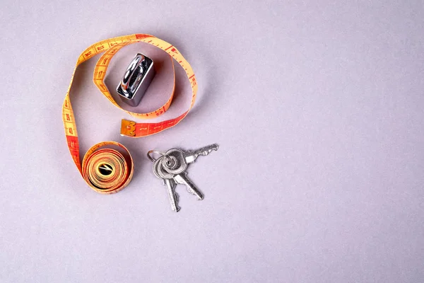 Meet tape en hangslot sleutel op een grijze achtergrond. Gewichts observatie, gezonde levensstijl en fitness concept — Stockfoto