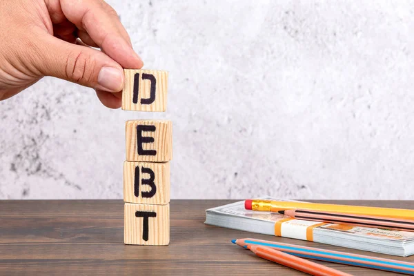 Schulden. Holzbuchstaben, Geld und Bleistifte — Stockfoto