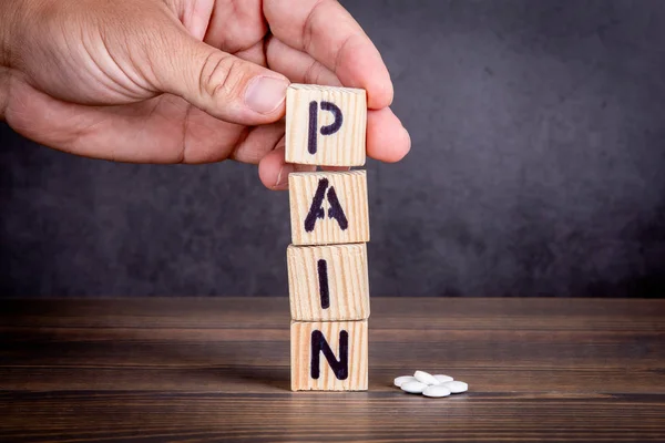 Έννοια του πόνου. Ξύλινα γράμματα και λευκά χάπια — Φωτογραφία Αρχείου
