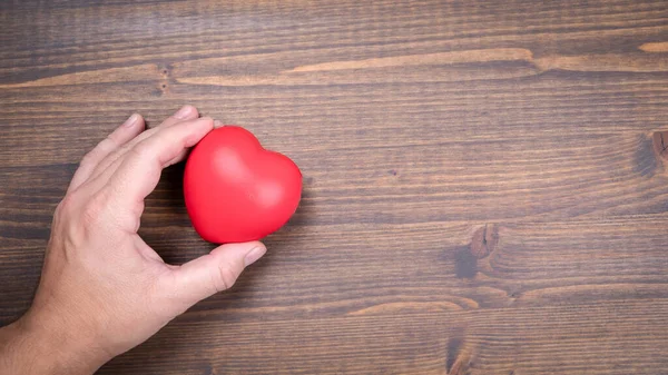 Καρδιά σχήμα μπάλα στρες σε ένα mans χέρια σε ένα ξύλινο φόντο — Φωτογραφία Αρχείου