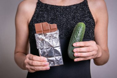 Diyet konsepti. Tatlı ve besleyici çikolata ve diyet salatalık arasında seçim yapmak.