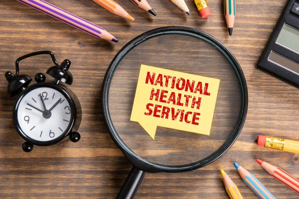 Concetto di servizio sanitario nazionale. Lente d'ingrandimento nera, bolla vocale e matite colorate — Foto Stock