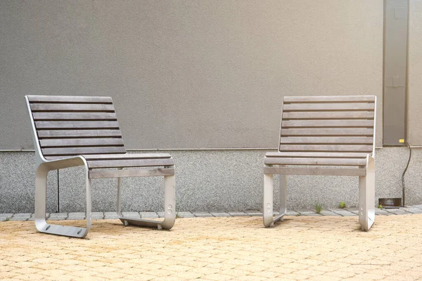 Grå träbänkar med metallkonstruktion i stadsmiljö för avkoppling vid grå vägg. Gula trottoaren — Stockfoto