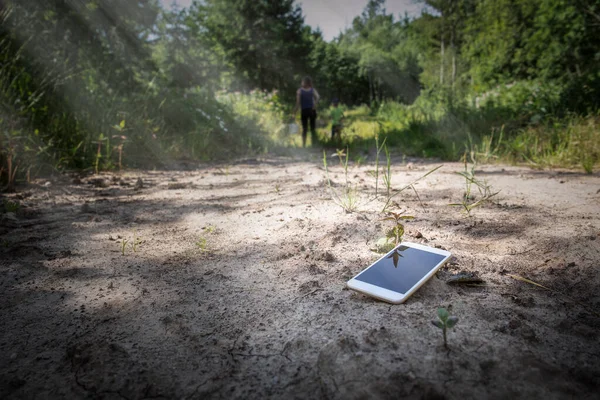 Lost smartphone on the ground, people in background. Geting lost in the forest