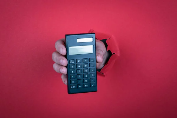 Calcolatrice nera in mano alla donna. sfondo carta rossa — Foto Stock