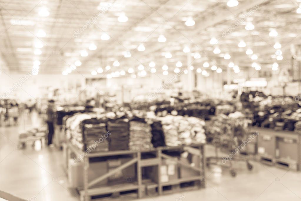 Vintage abstract blurred huge variety of items at clothing section with customer shopping in modern distribution warehouse. Defocused background of storehouse interior aisle and rows