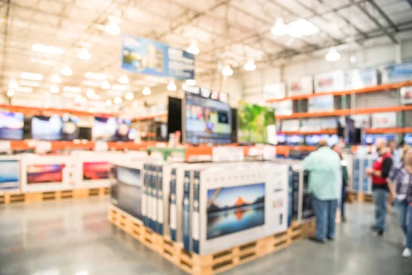 Electronic department store with bokeh blurred background. Television retail shop, TVs display on shelf at wholesale store. Defocused warehouse interior technology aisle, shelves and customer shopping