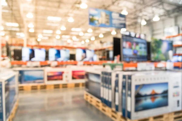 Electronic department store with row of TVs on shelves display. Television retail shop, TVs shelf wholesale store. Defocused warehouse interior technology aisle, inventory, export, business concept.