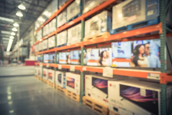 Vintage blurred electronic department store with row of TVs and boxes on shelves display from floor to ceiling. Television retail shop, wholesale store. Defocused warehouse interior technology aisle