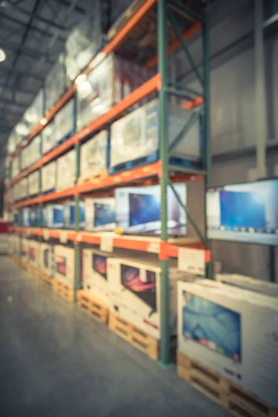 Vintage blurred electronic department store with row of TVs and boxes on shelves display from floor to ceiling. Television retail shop, wholesale store. Defocused warehouse interior technology aisle