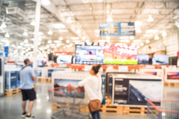 Blurred customer shopping at electronic department, television retail shop. TVs display on shelf at wholesale store in USA. Defocused warehouse interior technology aisle, shelves, bokeh background
