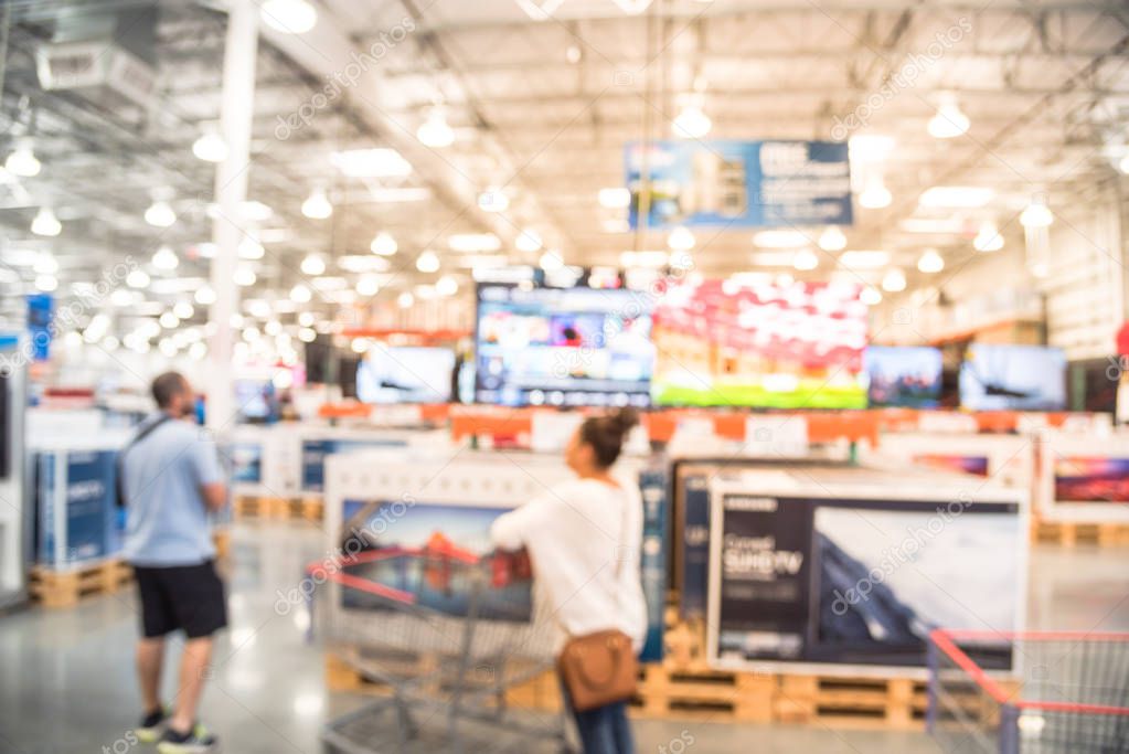 Blurred customer shopping at electronic department, television retail shop. TVs display on shelf at wholesale store in USA. Defocused warehouse interior technology aisle, shelves, bokeh background