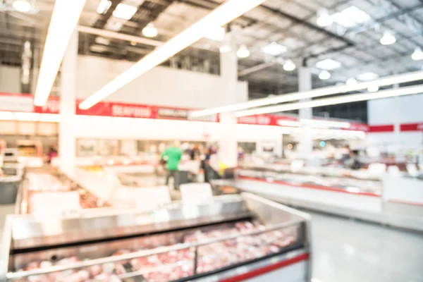 Blurred image customers shopping for fresh raw beef, pork, chicken, fish at meat department in wholesale store in US. Fully loaded shelves with variety of meat slices in boxes in a large supermarket.