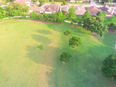Aerial view huge park near residential houses in Houston, Texas, USA. Green urban recreation with long pathway surrounds with green tree. Tightly packed homes neighborhood and driveways flyover clipart