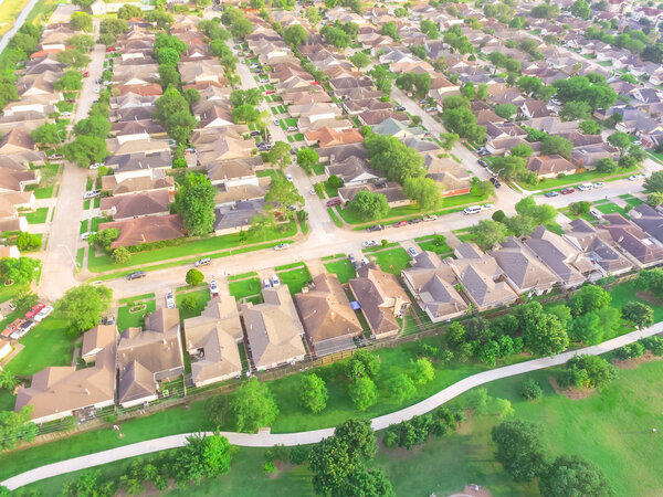 Aerial view huge park near residential houses in Houston, Texas, USA. Green urban recreation with long pathway surrounds with green tree. Tightly packed homes neighborhood and driveways flyover