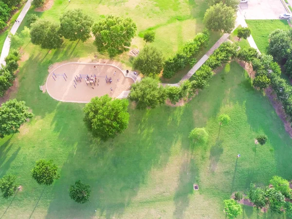 Aerial view kids playground and parking lot at Harwin park in Houston, Texas. An elevated view of slides and swings in the park surrounded by green trees. Children outdoor play and recreation concept.