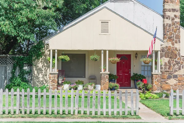 Modest house with chimney in historic downtown district of Irving, Texas, USA. Classic wooden fence with well-groomed landscape, haning flower pots, big tree and proudly American flag waving