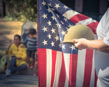 Vintage sesi beyaz bir usta gururla holding askeri Birinci Dünya Savaşı kask (M1 kask) ve bize bayrak. 4 Temmuz veya kıdemli gün ikinci Dünya Savaşı, modern savaşlar posteri. İnsan izlerken ile geçit töreni sırasında Amerikan askeri asker