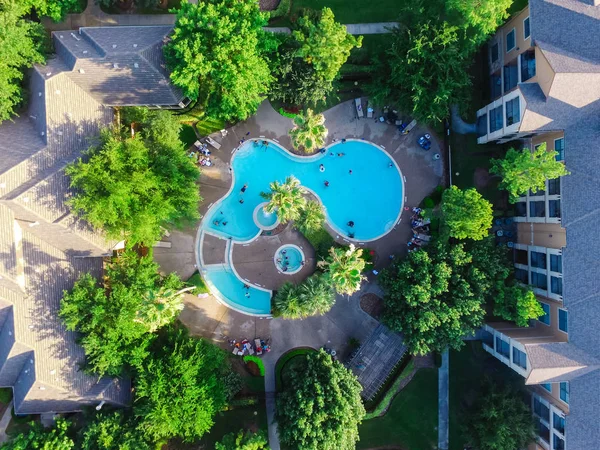 Aerial view of swimming pool in a typical multi-level apartment living in Houston, Texas, US at sunset. It surrounded by green garden, foldable chairs furniture and unidentified swimming kids.