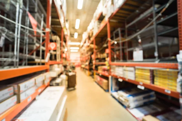 Blurred large hardware store. Defocused interior home improvement retailer with racks of flooring tools and material as wire and metal shelving, moulding, wood trim, laminate floor up to ceiling.