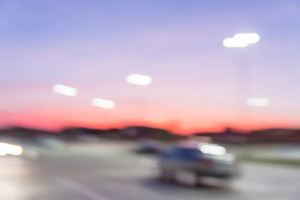 Blurred abstract parking lot at modern commercial strip in Irving, Texas, USA. Exterior mall shopping center complex with row of cars in outdoor uncovered parking, bokeh light poles in background